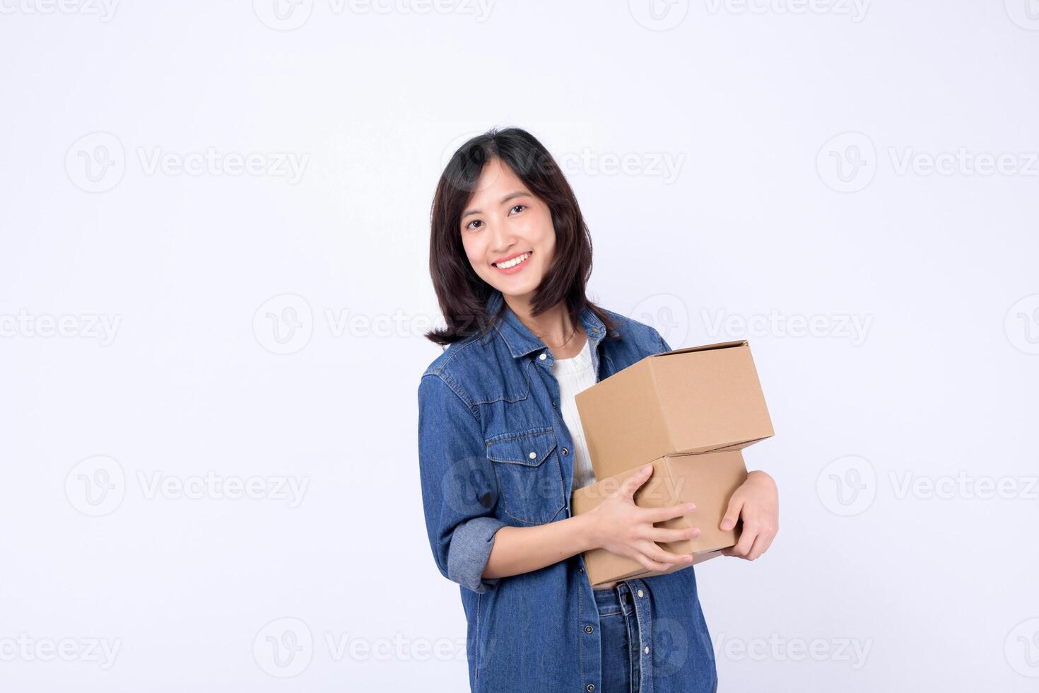 Southeast asian woman smiling happily while shopping online holds two cardboard boxes in her arms wearing casual denim clothes against plain white background photo