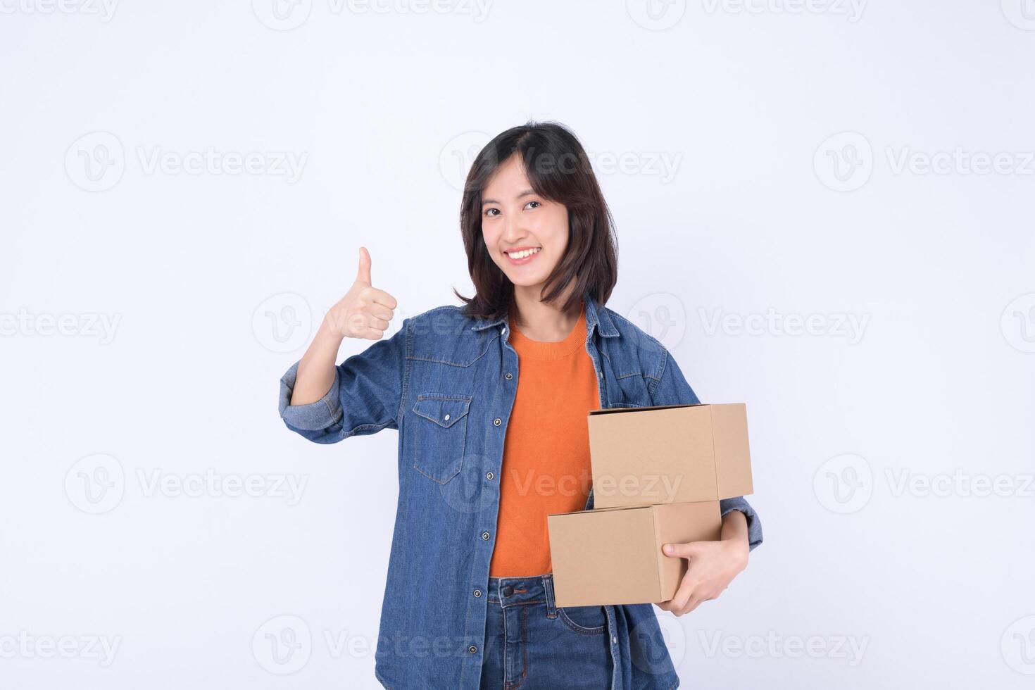 Southeast asian woman is happily shopping online holding two cardboard boxes and giving thumbs up gesture showing satisfaction and confidence in her purchase photo