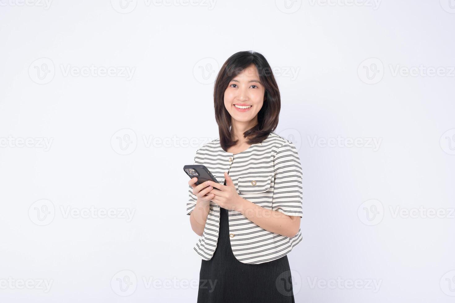 Southeast Asian woman smiling while using mobile phone for internet application in casual outfit on white background with positive expression and modern technology photo