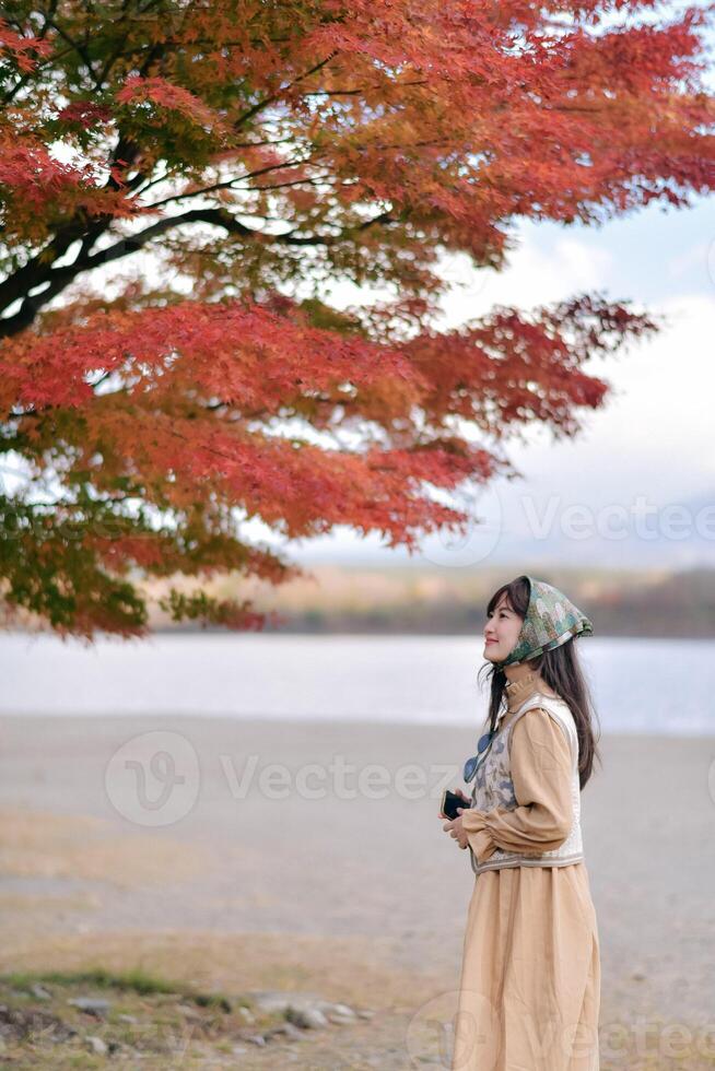 Southeast asian woman enjoys travel concept by admiring vibrant autumn leaves near calm lake, expressing peaceful and reflective emotions in serene natural setting photo
