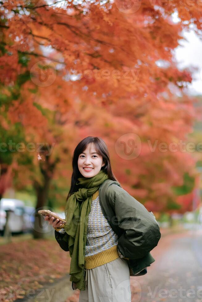 Southeast asian woman smiling outdoors with autumn leaves in background wearing green scarf and jacket enjoying fall season photo
