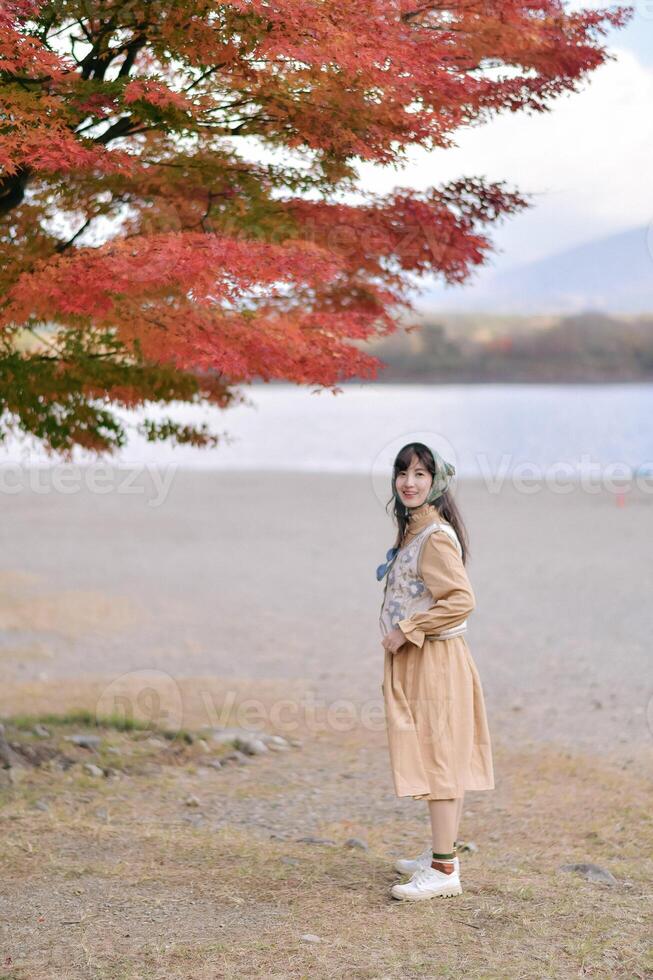 Southeast asian woman enjoys travel concept standing near lake with autumn red leaves above her creating peaceful and joyful outdoor scene in nature photo