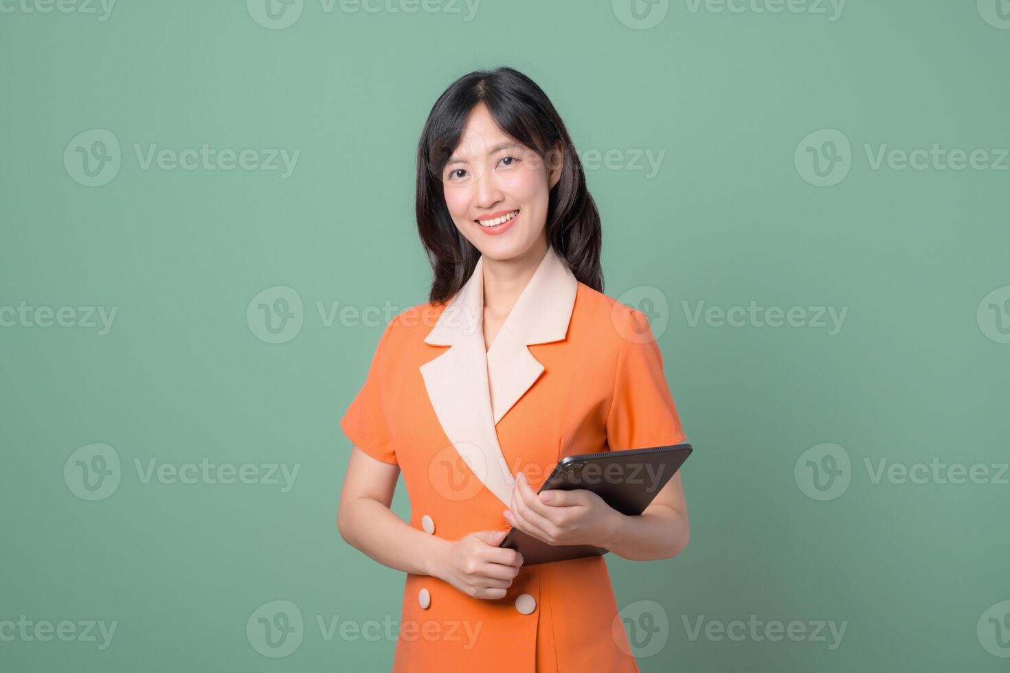 Southeast Asian woman smiling while holding tablet, standing against green background, representing internet technology and modern communication in professional setting photo