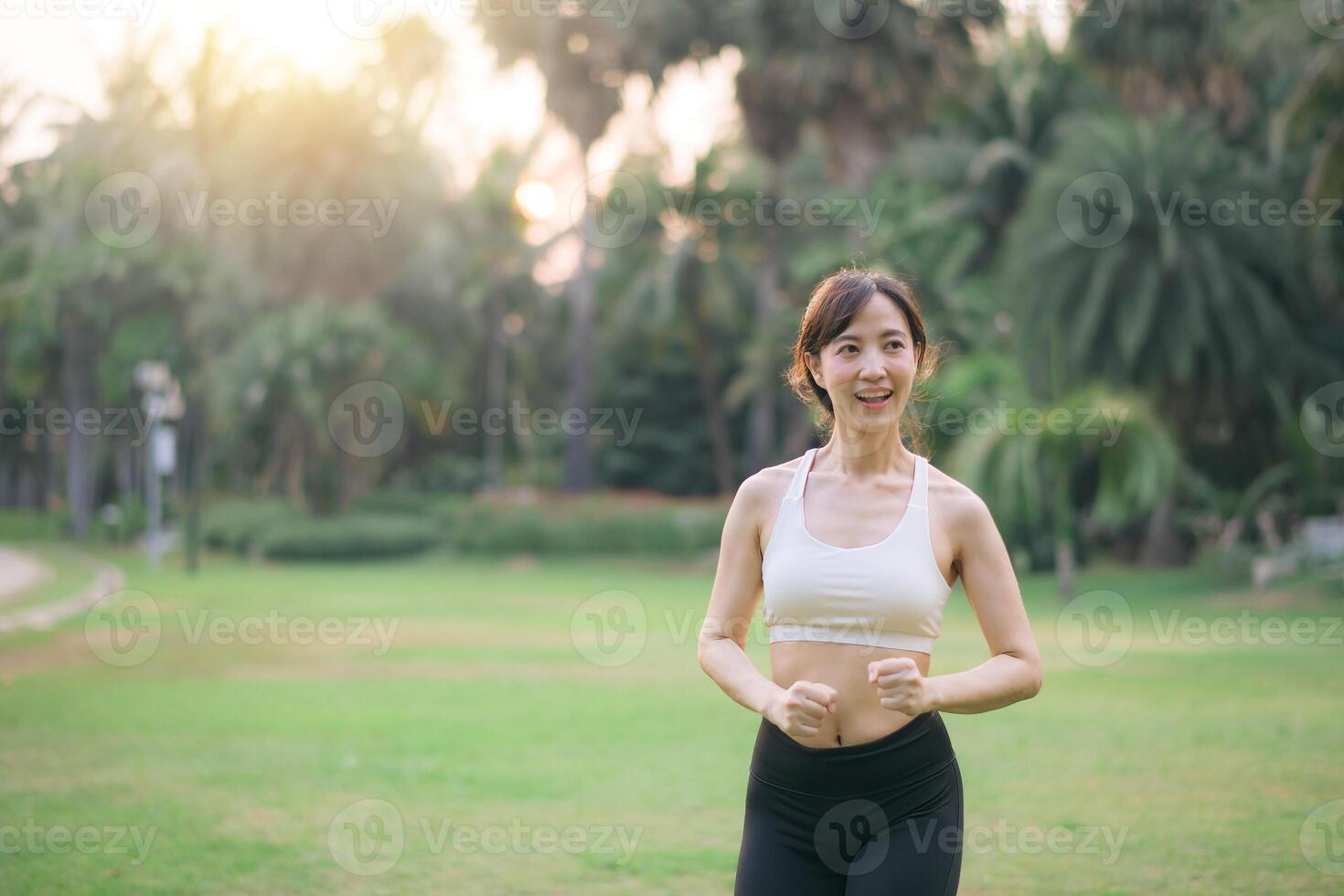 Southeast asian woman enjoying wellness and healthy lifestyle concept while exercising outdoors in park with joyful expression and natural green background photo