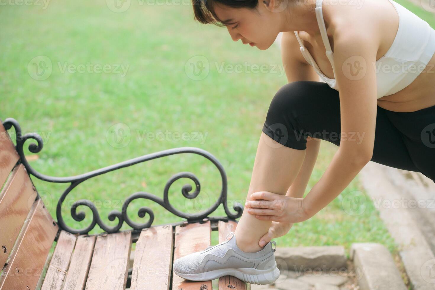 Southeast asian woman in activewear holding her ankle on park bench shows wellness and healthy lifestyle concept with exercise outdoors and determination in fitness routine photo