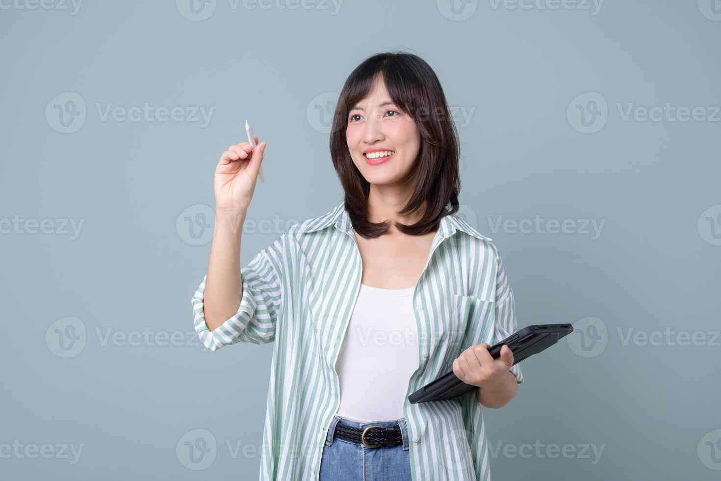 Southeast asian woman holding tablet and stylus smiling while using internet technology for creative work against plain background photo