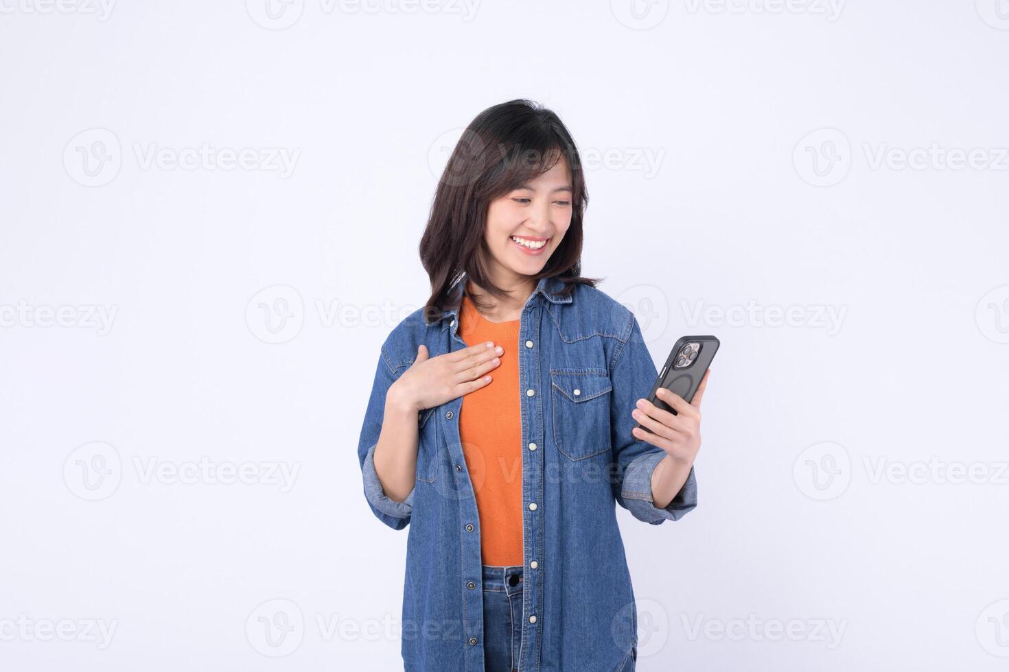 Southeast asian woman happily uses mobile phone to access internet application while standing against plain background showing joy and engagement with technology photo