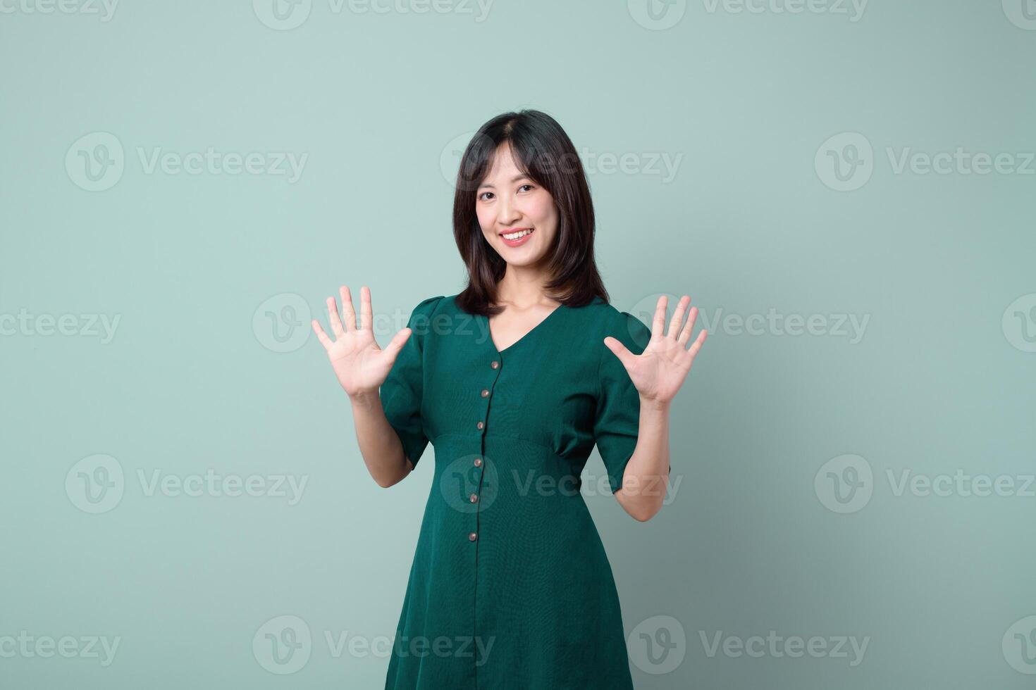 Southeast Asian woman in green dress smiling and showing ten fingers for advertising with happy and confident expression on light blue background photo