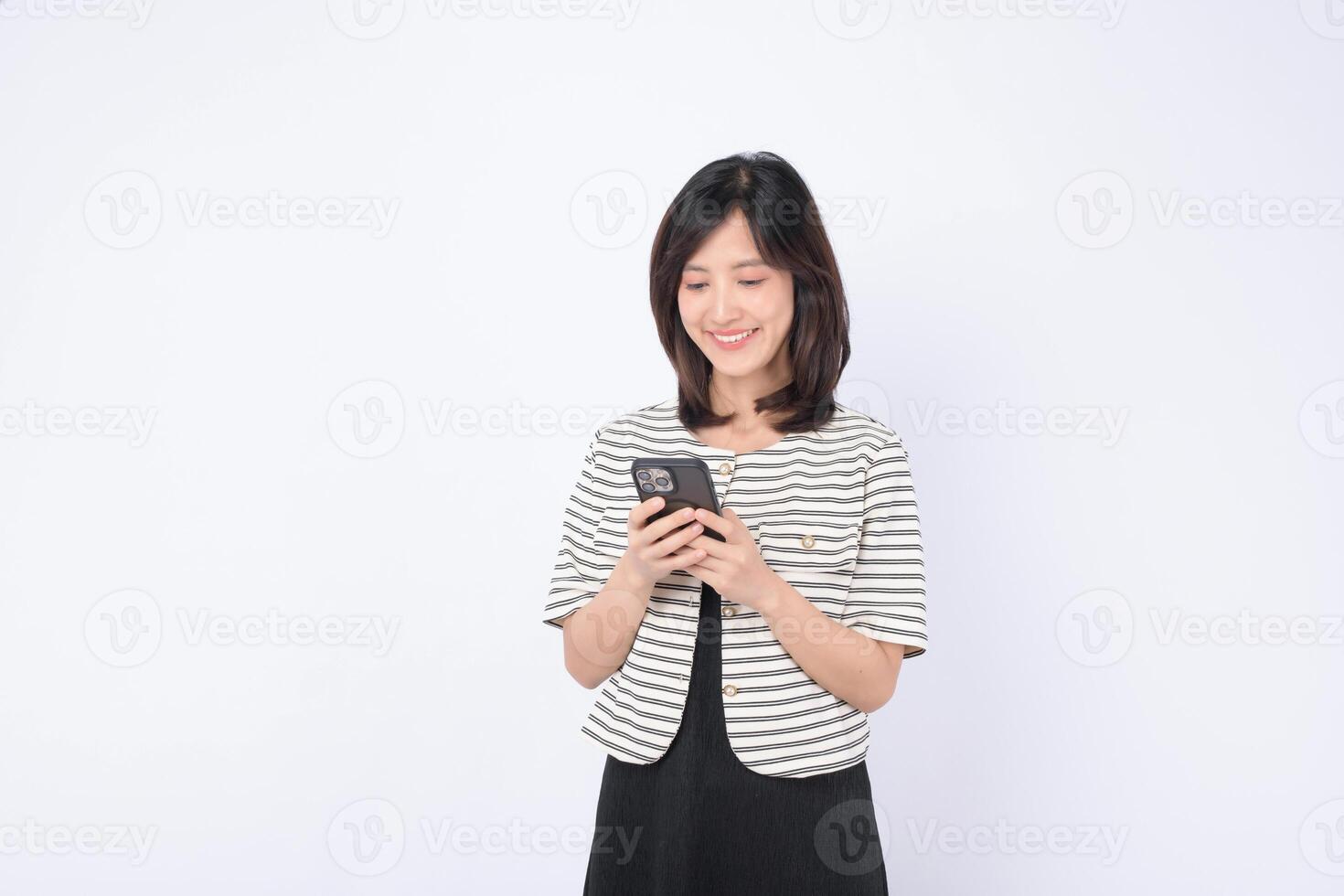 Southeast asian woman happily using mobile phone to access internet application in bright setting with casual striped jacket and black dress photo