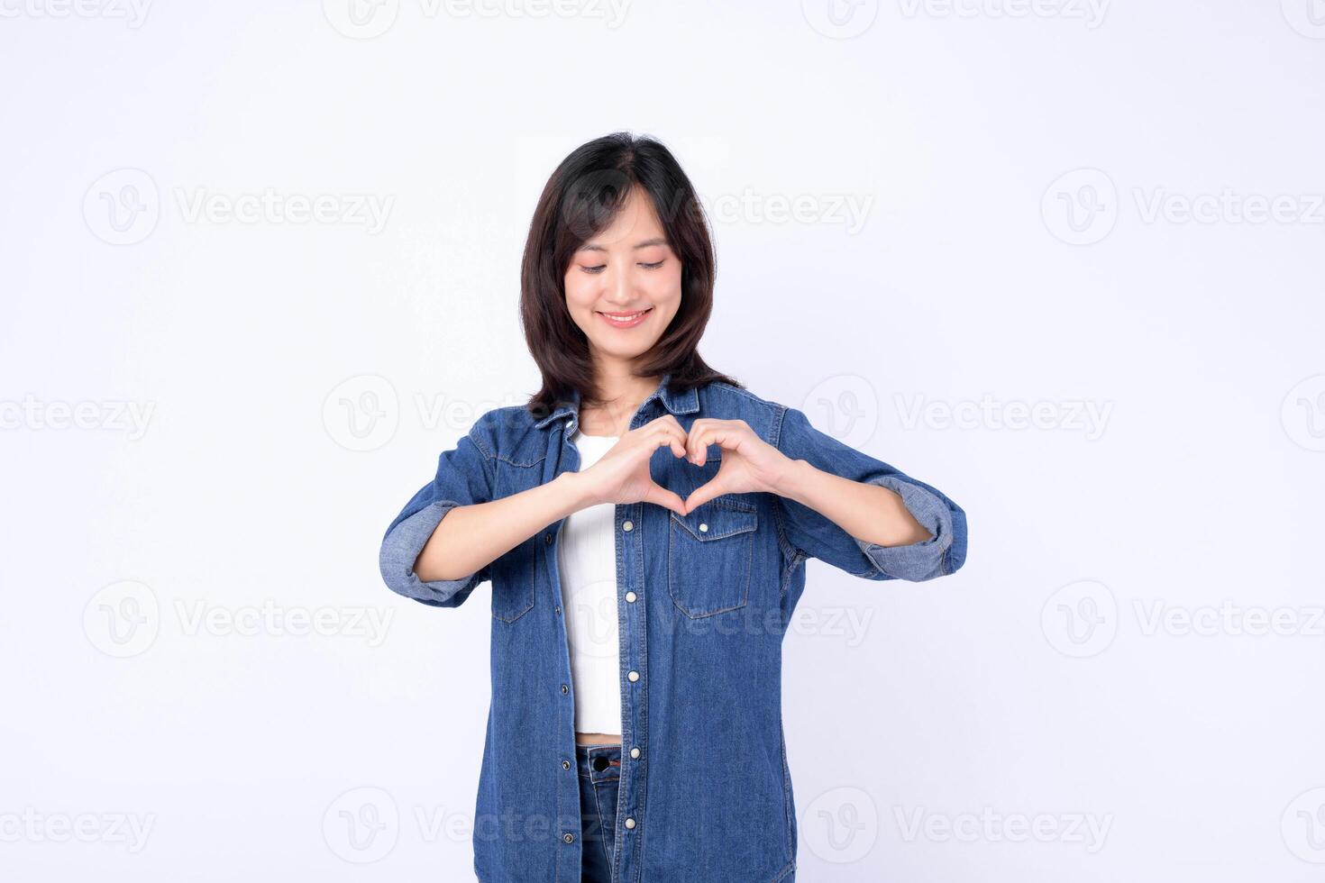 Southeast asian woman wearing denim shows heart shape with her hands smiling gently in bright advertising style portrait image photo