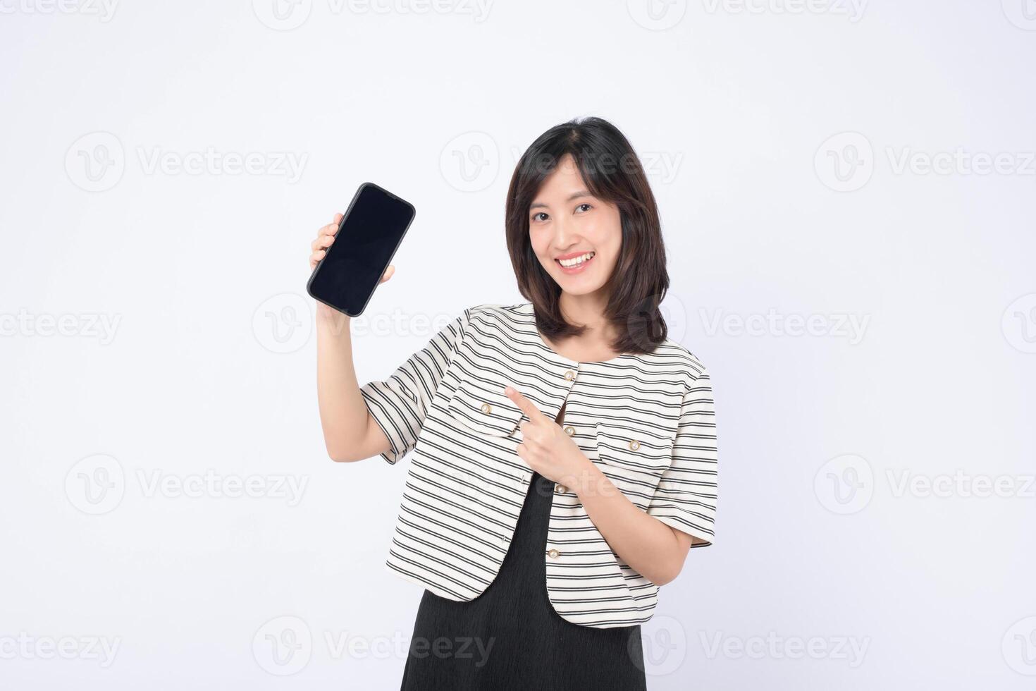 Southeast asian woman happily points at mobile phone screen showing internet application, demonstrating excitement and engagement with digital technology in bright setting photo