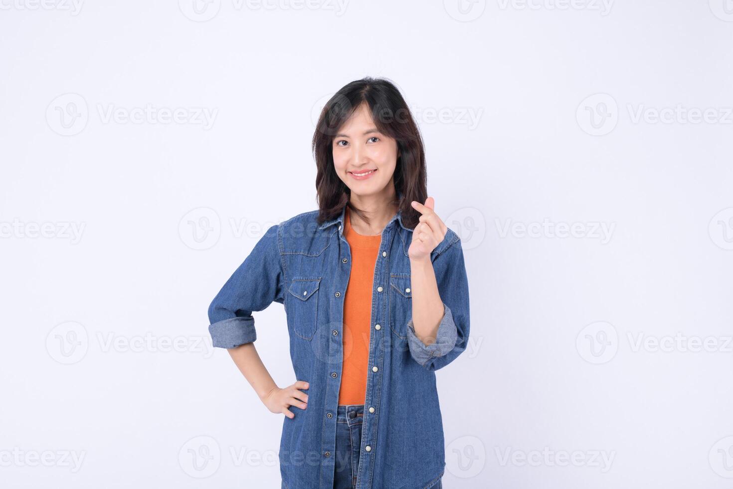 Southeast asian woman wearing denim jacket and orange shirt smiling and advertising with hand gesture in front of white background photo