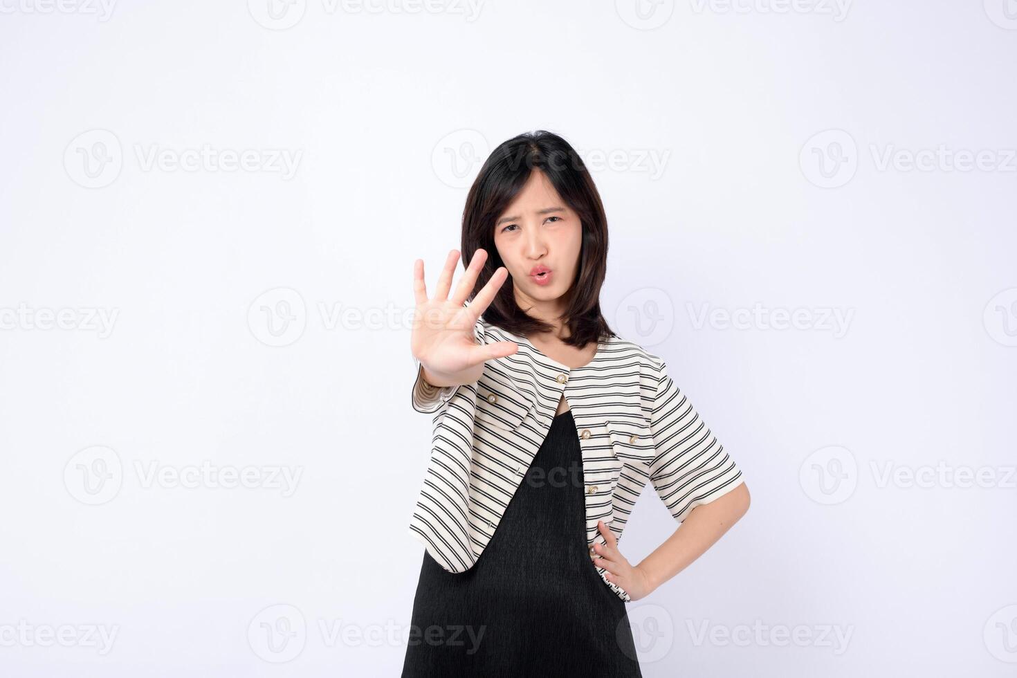 Southeast asian woman in advertising style poses with serious expression showing stop gesture with her hand in front of white background photo