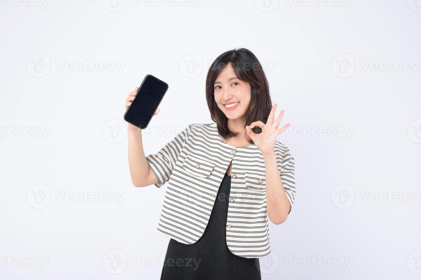 Southeast asian woman happily shows mobile phone with internet application on screen while making okay gesture expressing confidence and satisfaction photo
