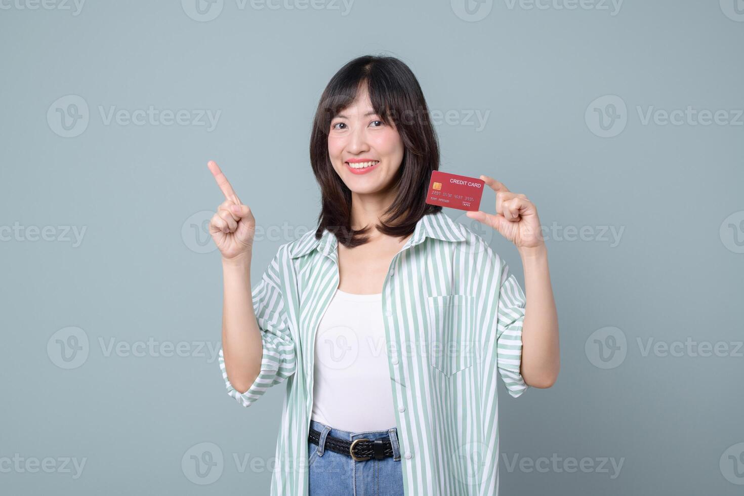 Southeast asian woman shopping online with credit card smiling and pointing up on gray background showing happiness and confidence photo