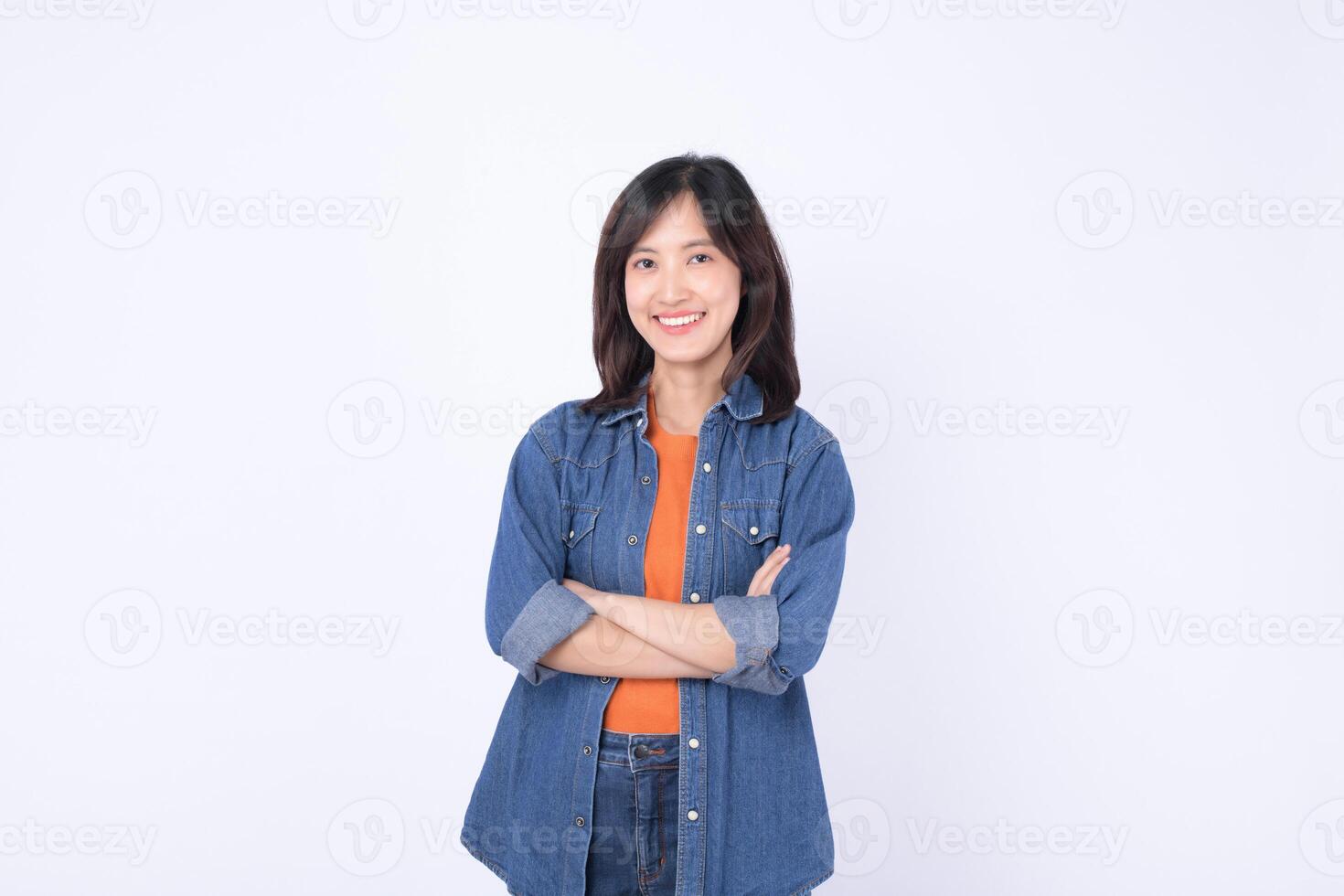 Southeast asian woman smiling confidently in casual denim clothing posing for advertising with arms crossed and bright cheerful expression photo