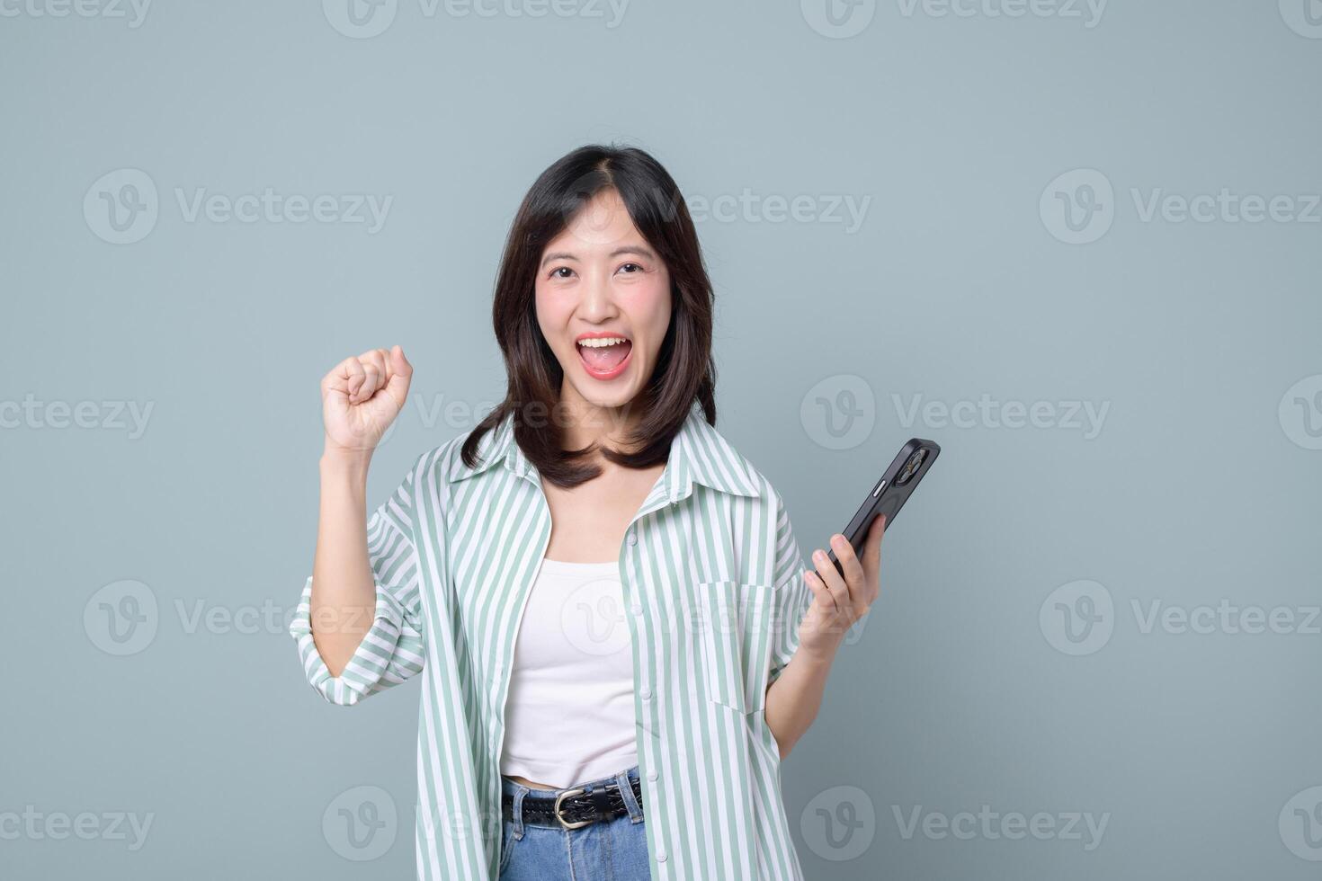 Happy southeast asian woman using mobile phone with internet connection enjoying mobile application in casual clothes with cheerful expression on plain background photo