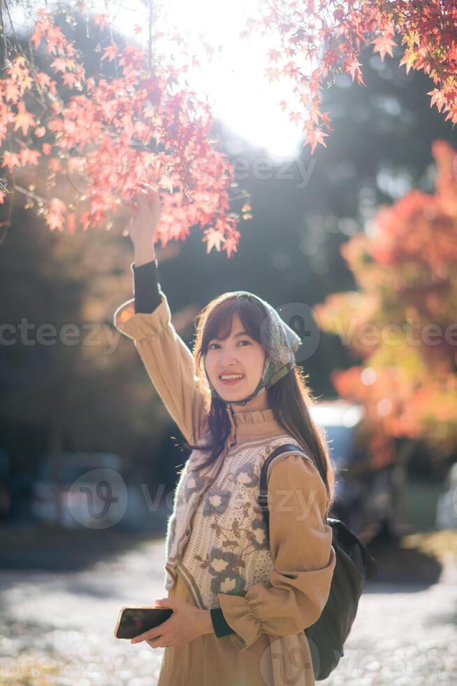Southeast asian woman enjoys travel concept by reaching for red autumn leaves with joyful smile outdoors in soft sunlight creating warm and peaceful atmosphere photo