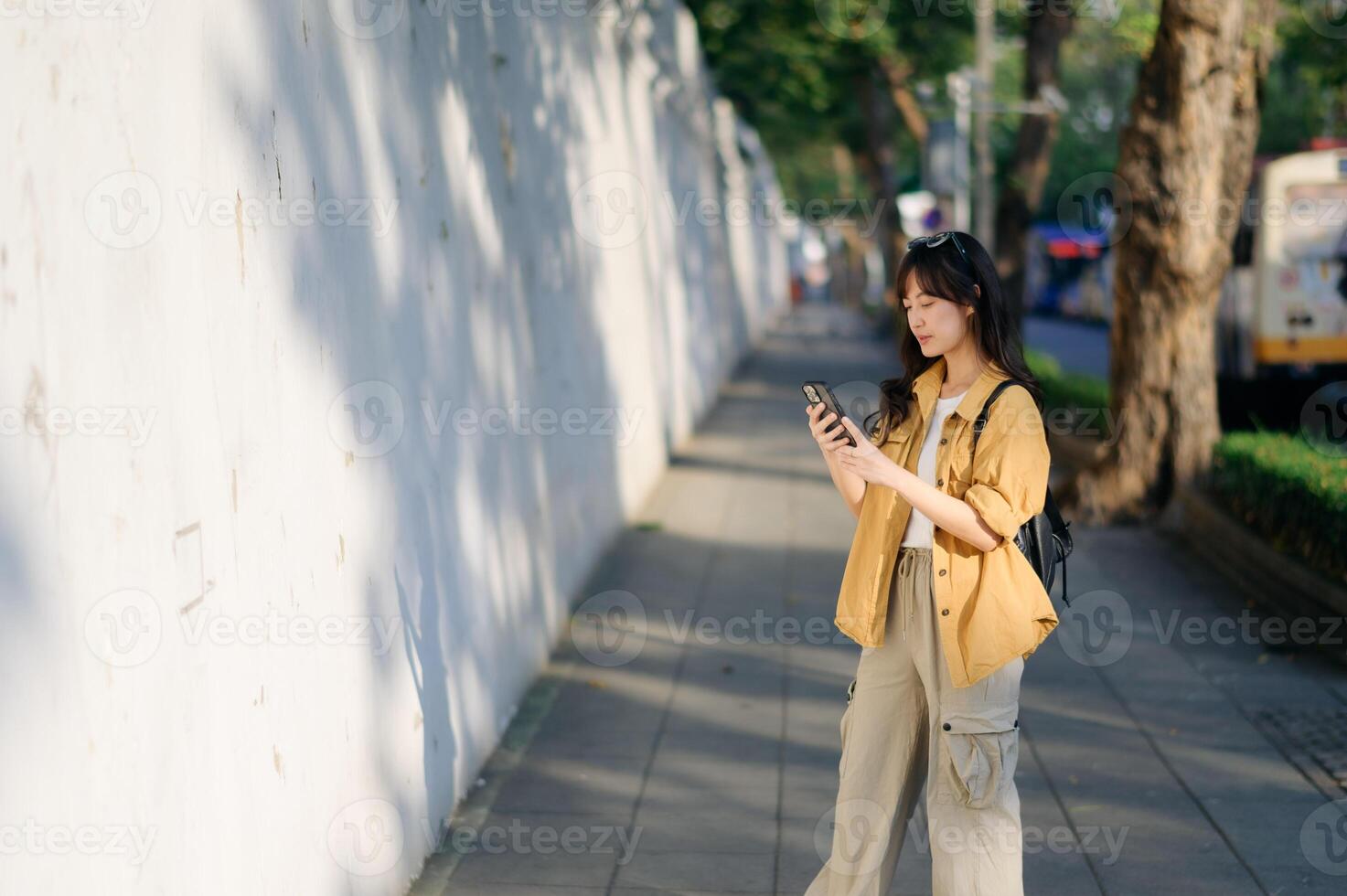Southeast asian woman enjoys travel concept by exploring city street while using her phone in casual outfit under warm sunlight creating calm and peaceful mood photo