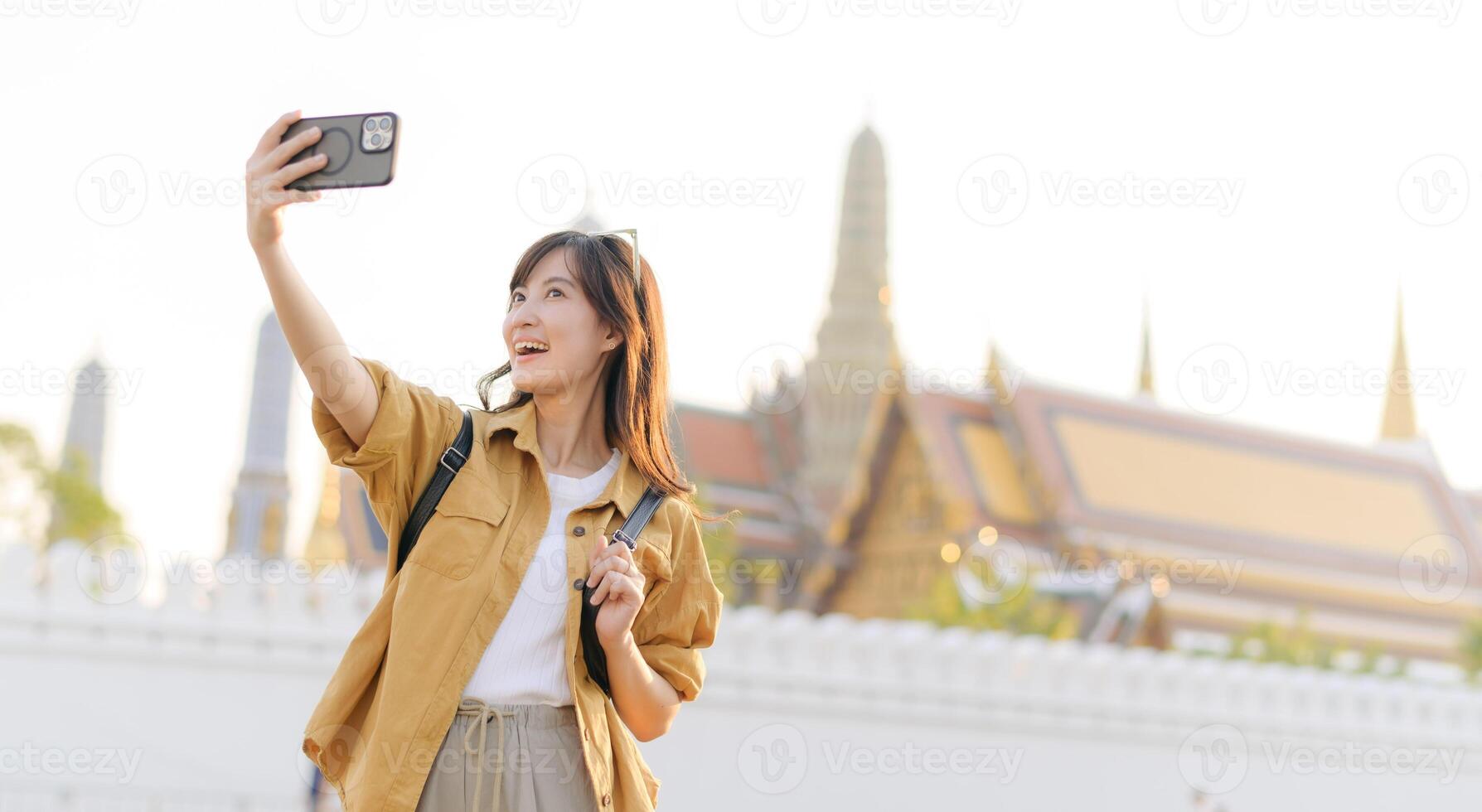 Southeast asian woman travel concept smiling taking selfie with smartphone at famous temple in bright daylight photo