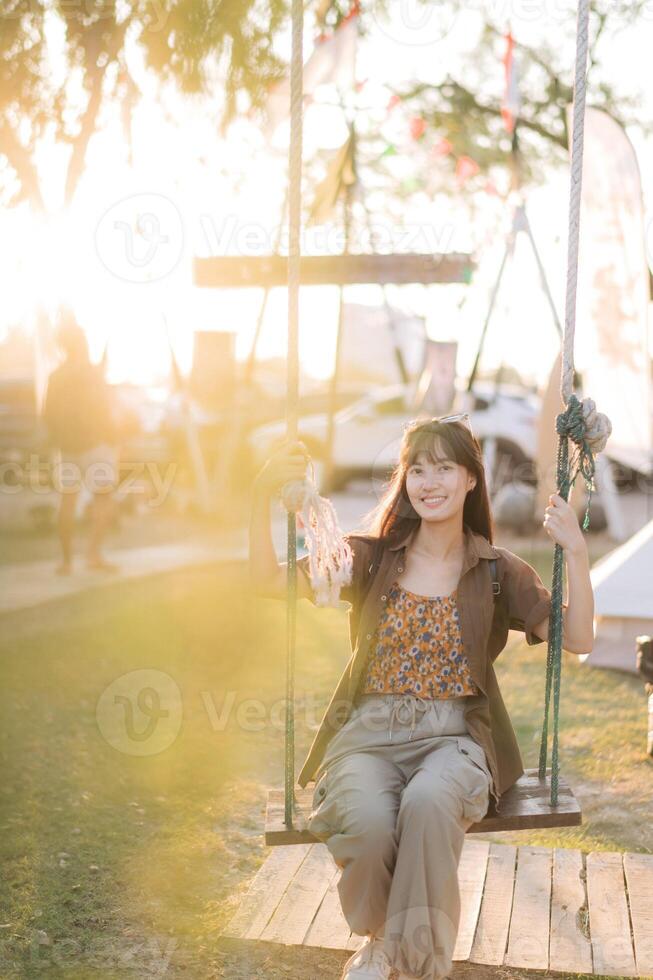 Southeast asian woman enjoys travel concept sitting on swing outdoors with warm sunlight creating joyful and relaxed atmosphere in natural park setting photo