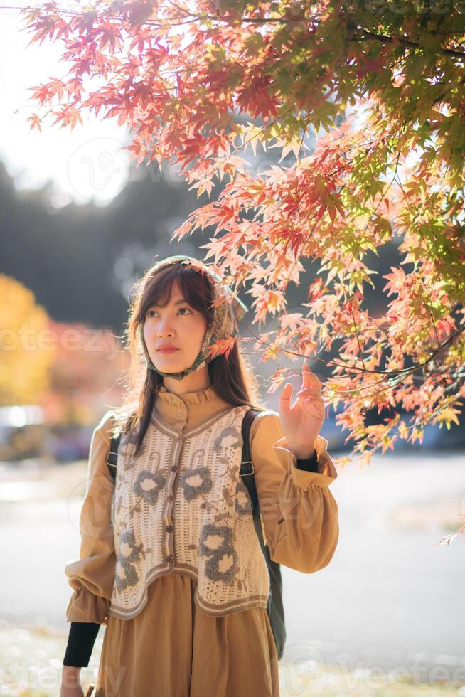 Southeast asian woman enjoys travel concept by admiring colorful autumn leaves outdoors in soft sunlight creating peaceful and warm atmosphere during her journey photo