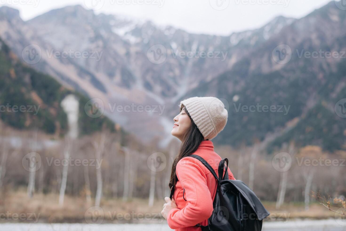 Southeast asian woman enjoys travel concept in mountains wearing warm hat and backpack with peaceful expression surrounded by nature and scenic landscape photo