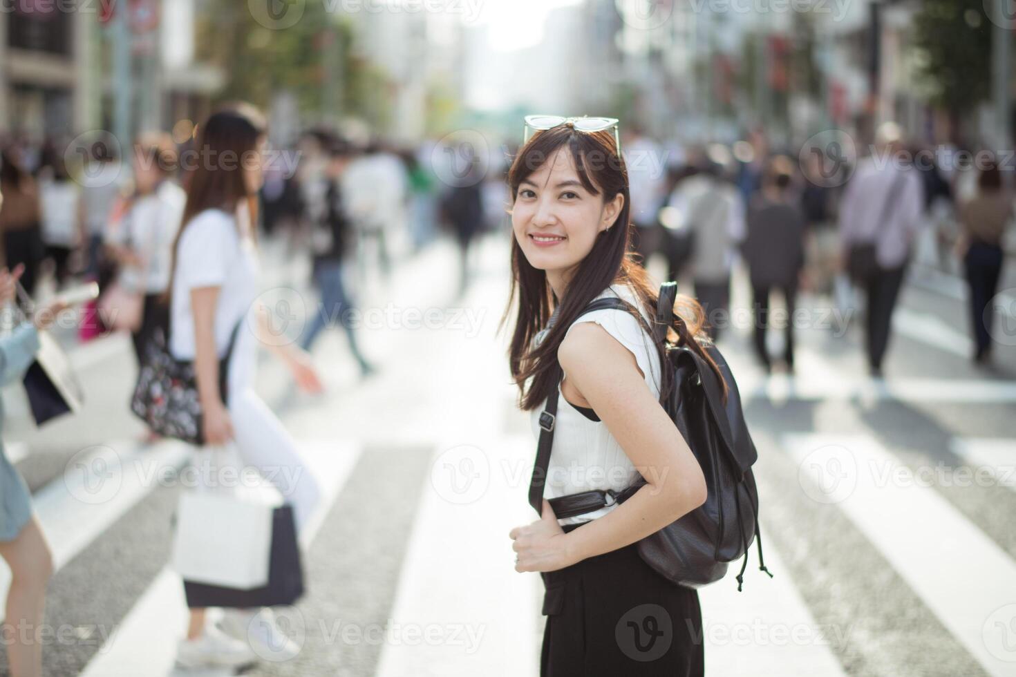 Southeast asian woman smiling with backpack walking on busy city street crosswalk in daylight photo