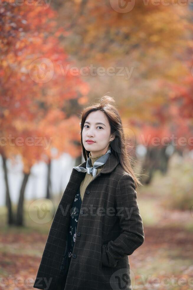 Southeast asian woman stands confidently in dark coat with autumn leaves in background creating warm and peaceful outdoor scene filled with natural beauty and calm expression photo