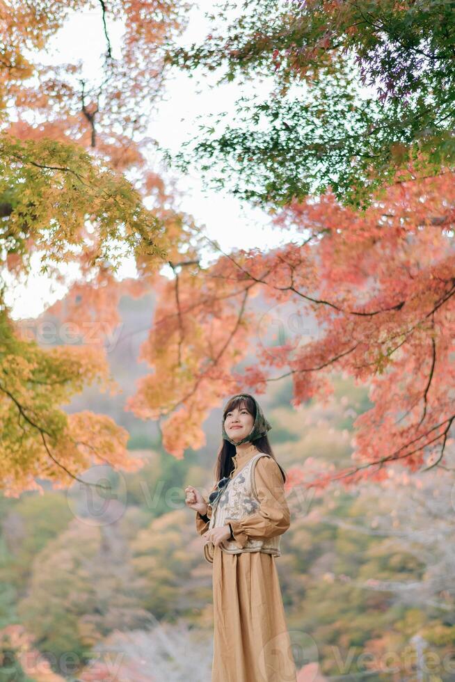 Southeast asian woman enjoys travel concept in autumn forest with colorful leaves around her creating peaceful and inspiring atmosphere for outdoor exploration and reflection photo