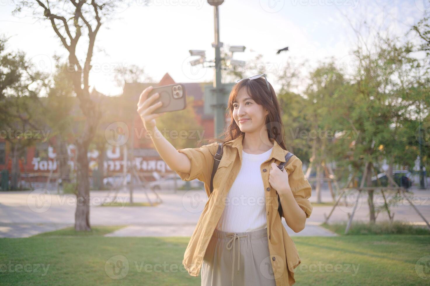 Southeast asian woman enjoys travel concept by taking selfie outdoors in park during golden hour with happy and relaxed expression on her face photo