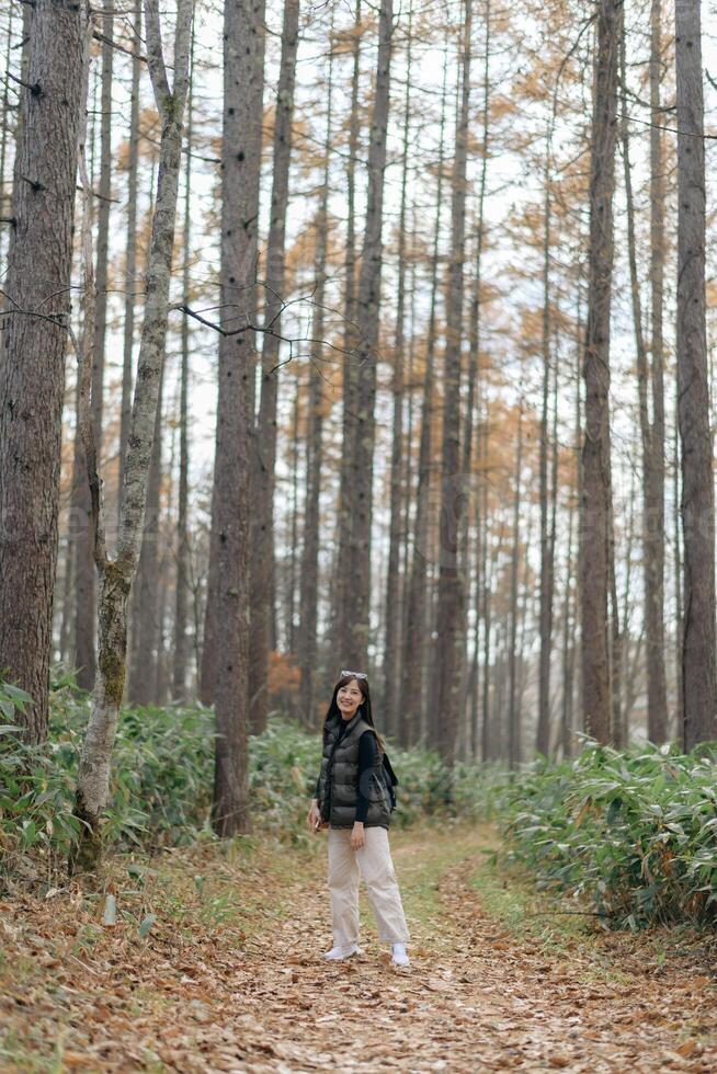 Southeast asian woman enjoys travel concept walking through tall tree forest path wearing casual clothes and backpack with happy and peaceful expression in nature photo