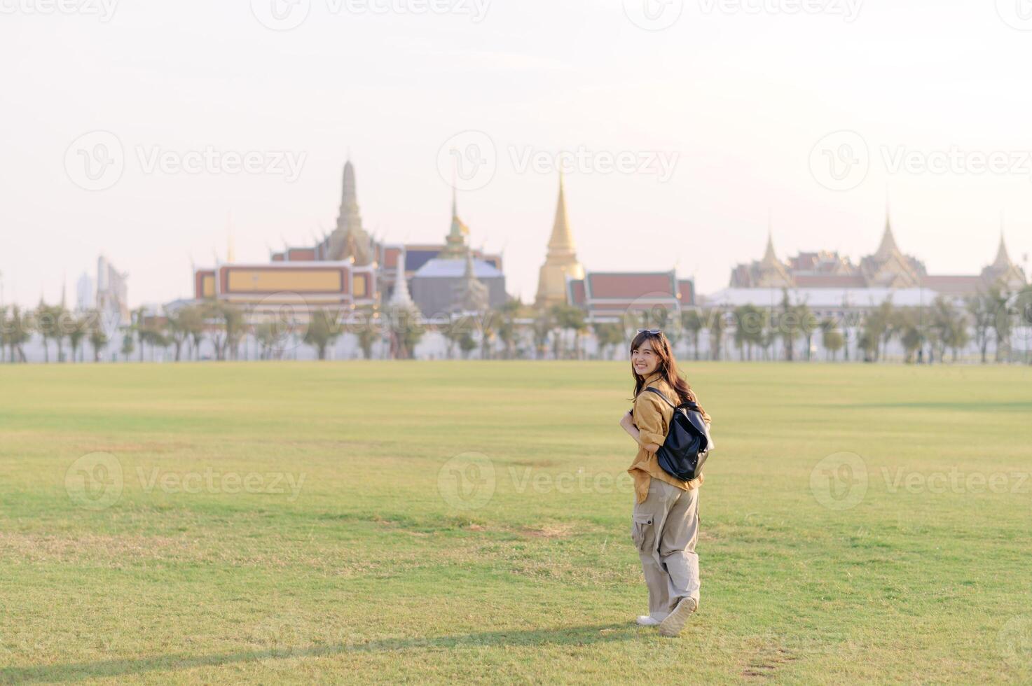 Southeast asian woman enjoys travel concept by exploring vast green field near historic temple complex, smiling happily as she embraces cultural adventure outdoors photo