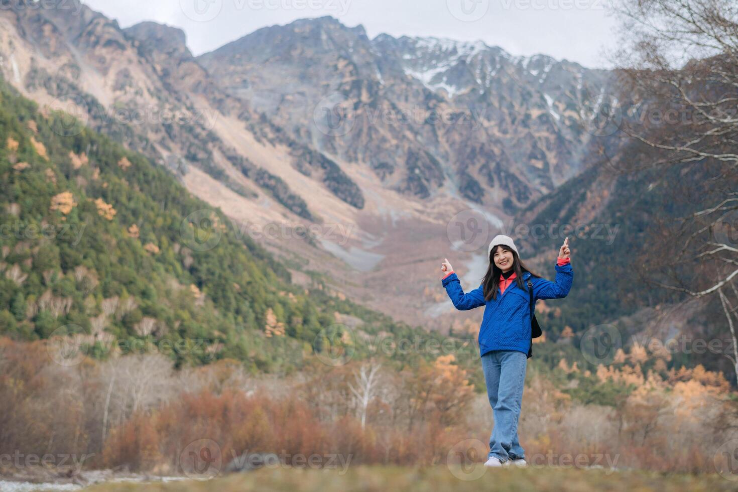 Southeast asian woman enjoys travel in mountainous landscape wearing blue jacket and hat, capturing concept of adventure and nature exploration with joyful expression photo