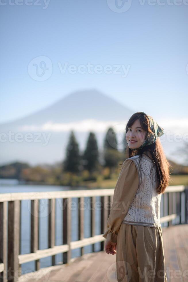 Southeast asian woman enjoys travel concept by lake with mountain view wearing headscarf and beige outfit smiling happily in peaceful outdoor setting photo