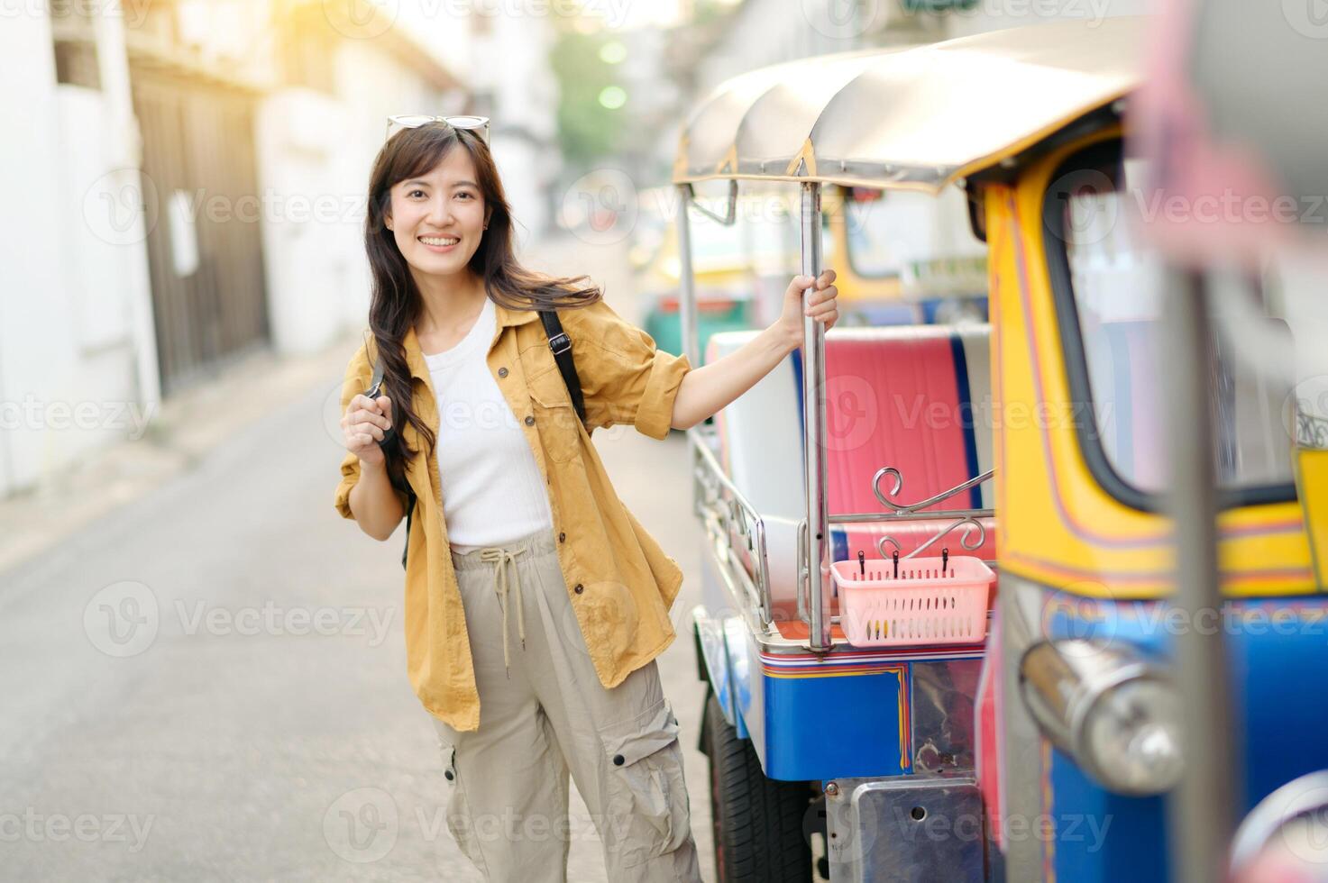 Southeast asian woman travel concept with happy smile stands beside colorful tuk tuk on sunny street ready for adventure and exploration in urban setting photo