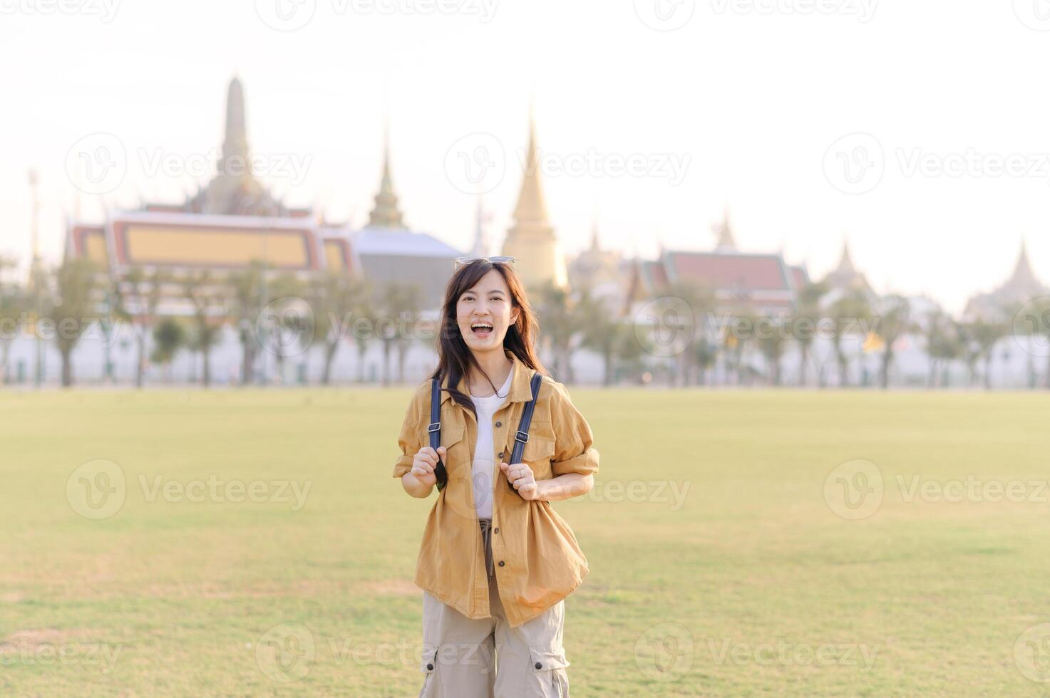 Southeast asian woman travel concept with joyful expression stands in large open field near historic temple buildings under bright daylight photo