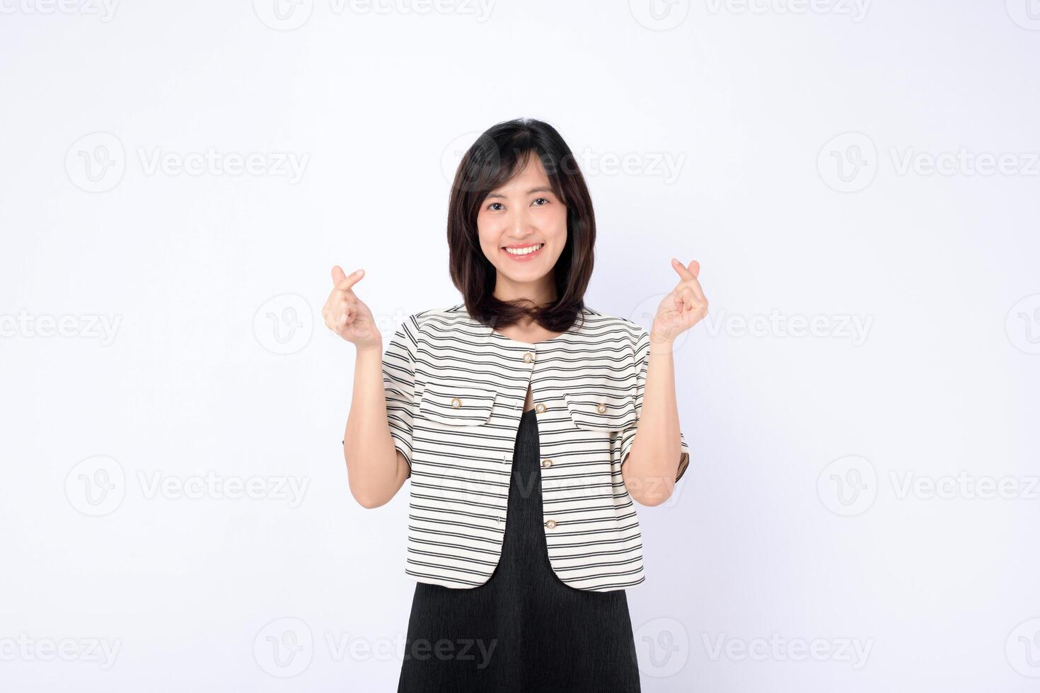 Asian woman smiling, making mini heart gesture with both hands, wearing striped jacket, standing against white background photo