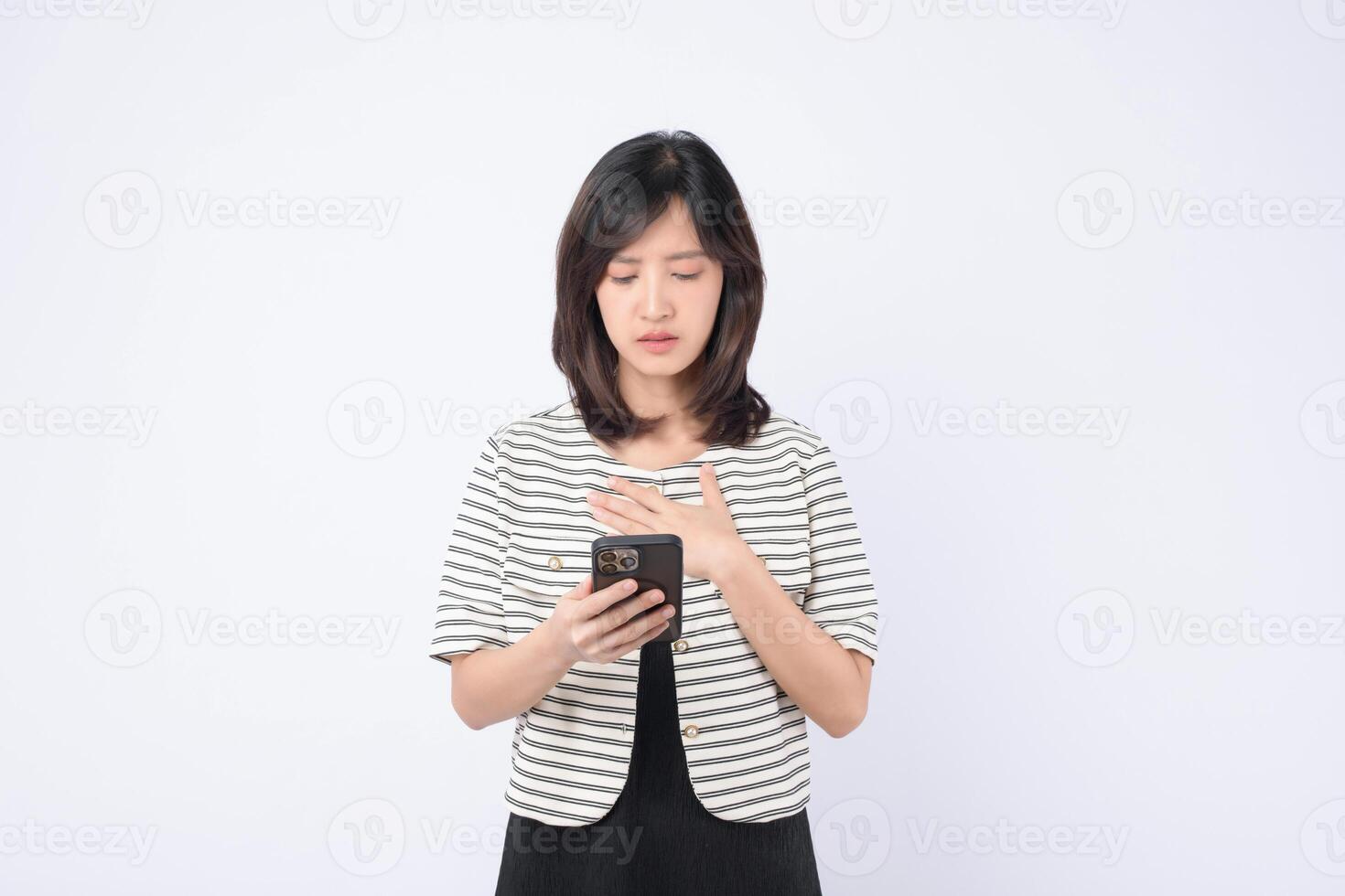 Southeast asian woman uses mobile phone with internet application looking concerned and focused on screen in bright studio setting with white background photo