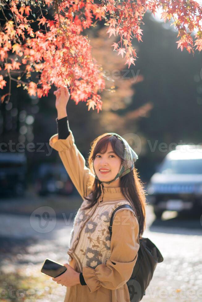 Southeast asian woman enjoys travel concept by reaching for red autumn leaves with joyful smile in soft sunlight creating warm and peaceful outdoor moment photo