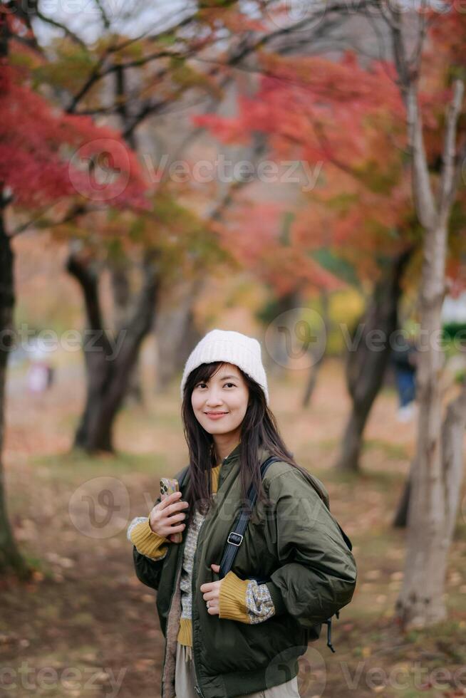 Southeast asian woman enjoys peaceful autumn walk wearing warm jacket and white knit hat surrounded by colorful fall leaves and soft natural light in serene park setting photo