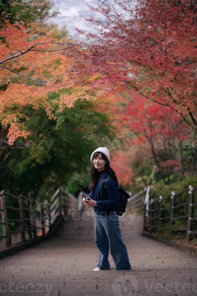 Southeast asian woman enjoys travel concept walking on stone stairway surrounded by colorful autumn trees with red and orange leaves creating peaceful and vibrant atmosphere photo