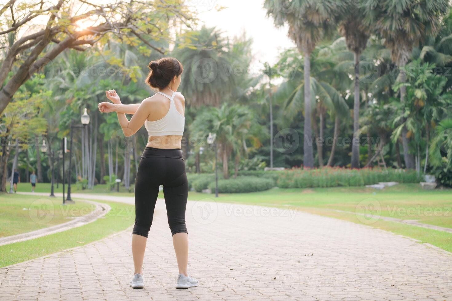 Southeast asian woman enjoying wellness and healthy lifestyle concept while doing exercise in park surrounded by green trees and sunlight in morning photo
