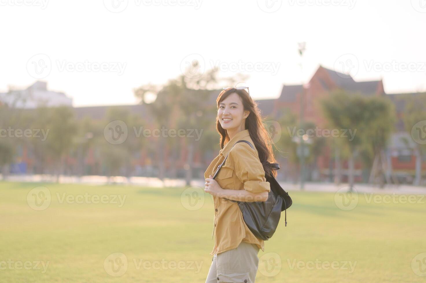 Asian woman traveler with backpack smiling in sunlight, enjoying outdoor adventure in city park, summer holiday vacation in Bangkok photo