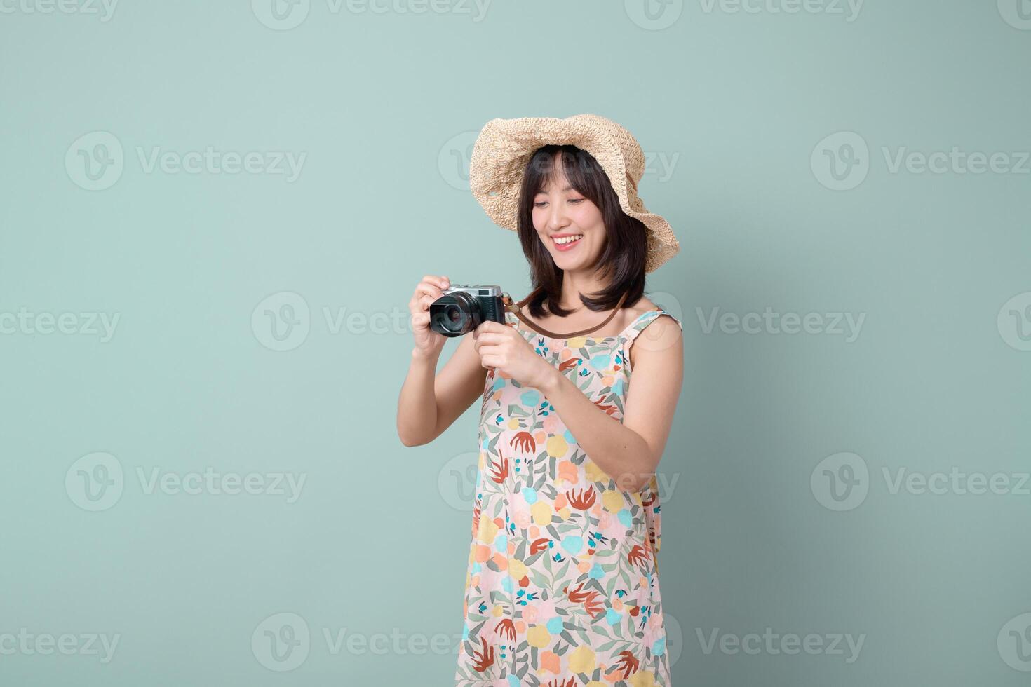 Southeast asian woman wearing floral dress and straw hat is happily holding camera capturing travel moments, embodying joyful travel concept with bright smile and relaxed pose photo