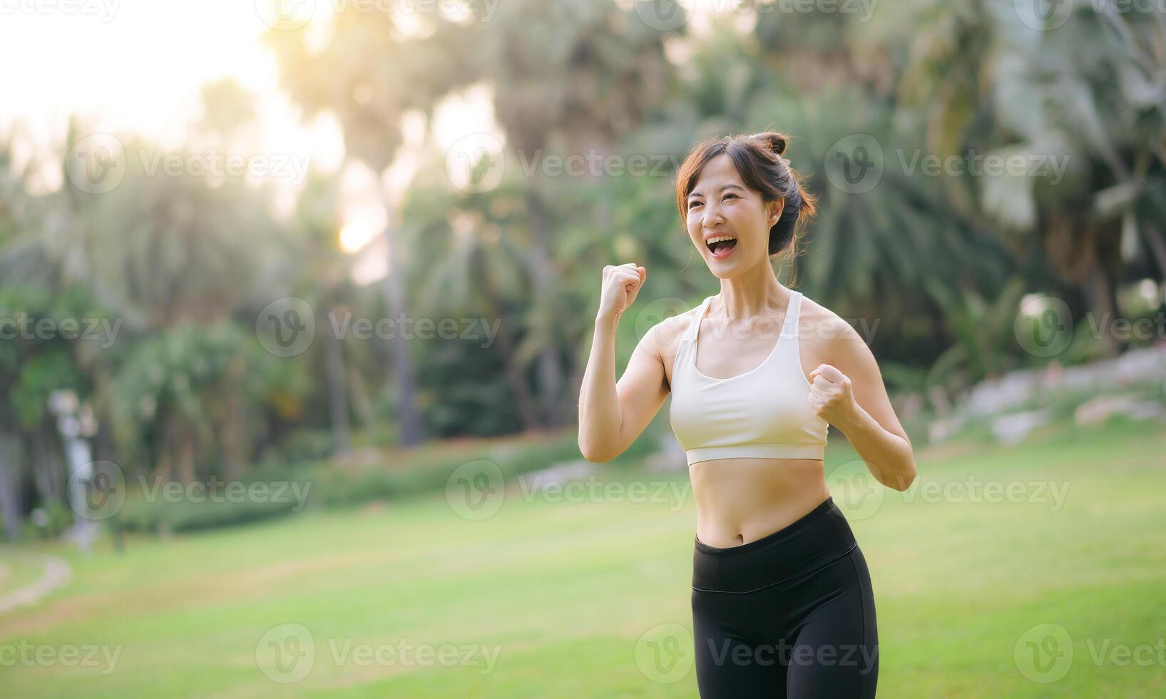 asian woman enjoying wellness and healthy lifestyle concept while exercising outdoors in park with joyful expression on her face photo