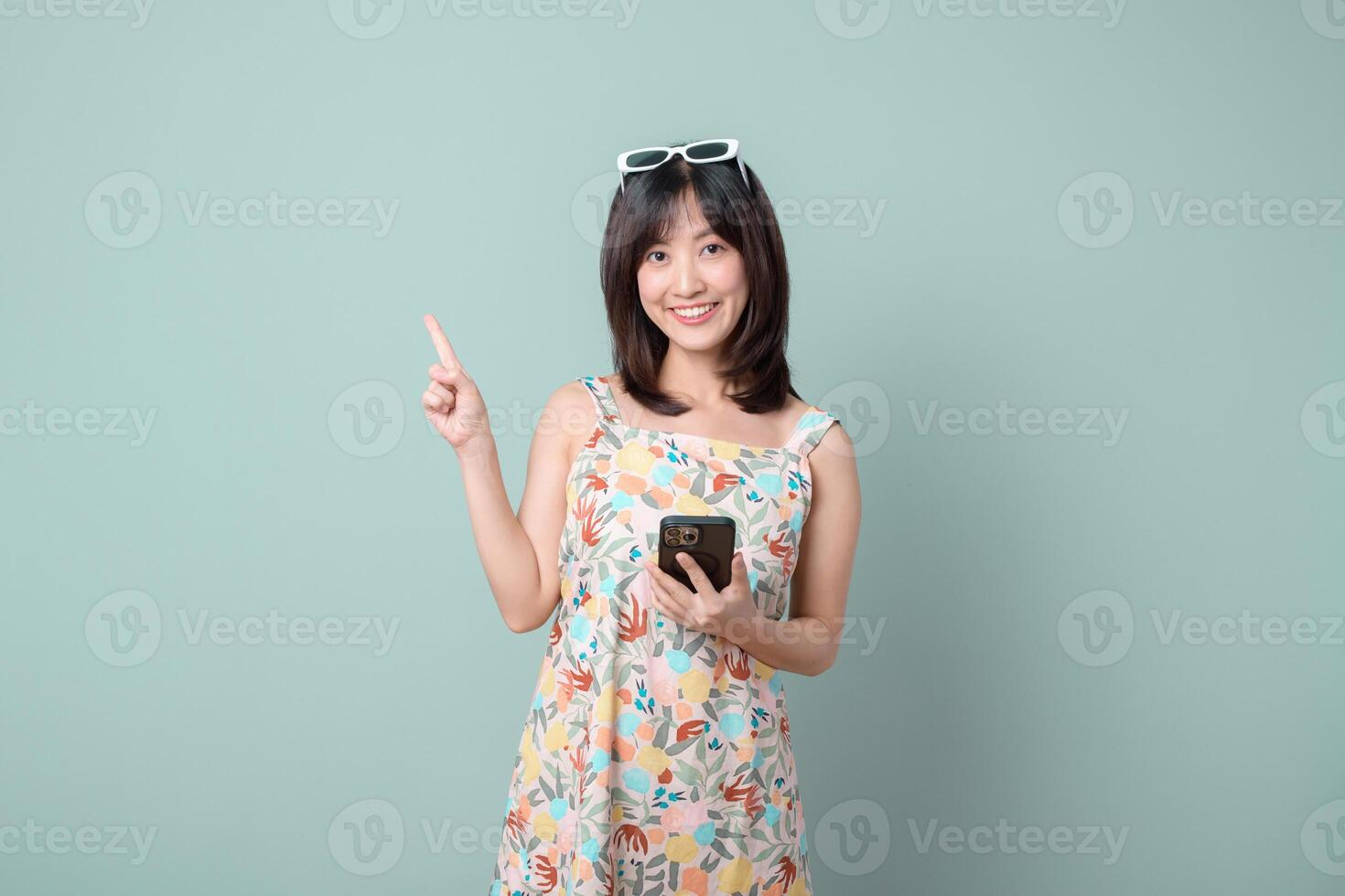 Southeast asian woman smiling happily while holding mobile phone and pointing up as if explaining internet application on pastel background photo