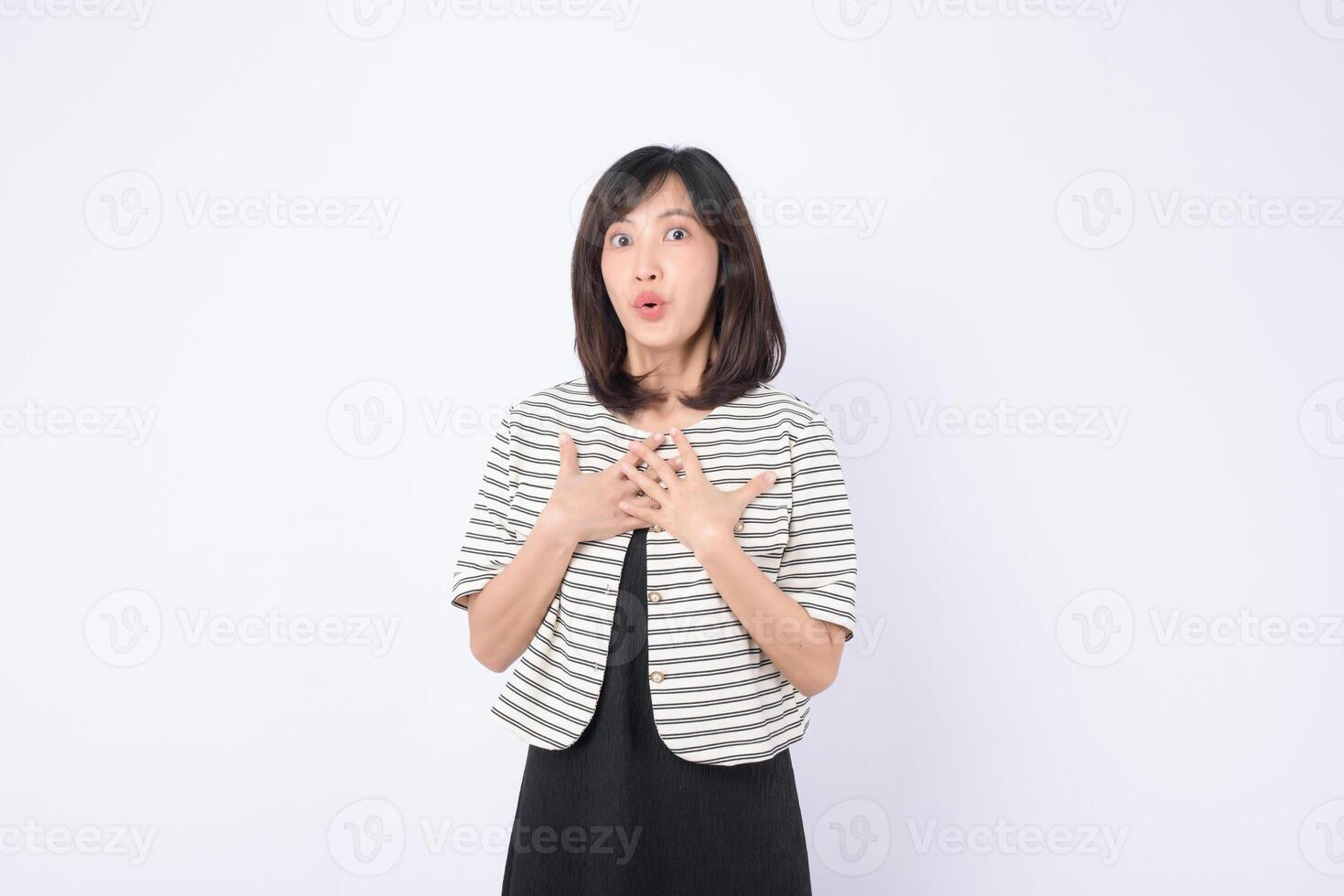 Surprised southeast asian woman with medium length black hair wearing striped jacket and black dress standing against white background with expressive face photo