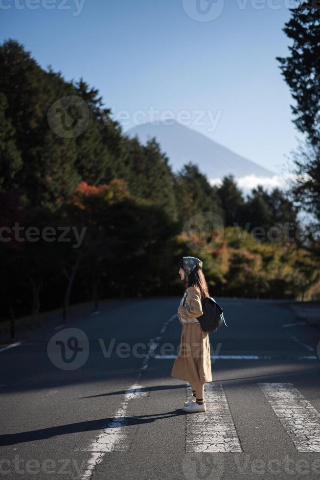 Southeast asian woman stands on quiet road surrounded by forest trees with mountain in background under clear blue sky creating peaceful and calm atmosphere photo
