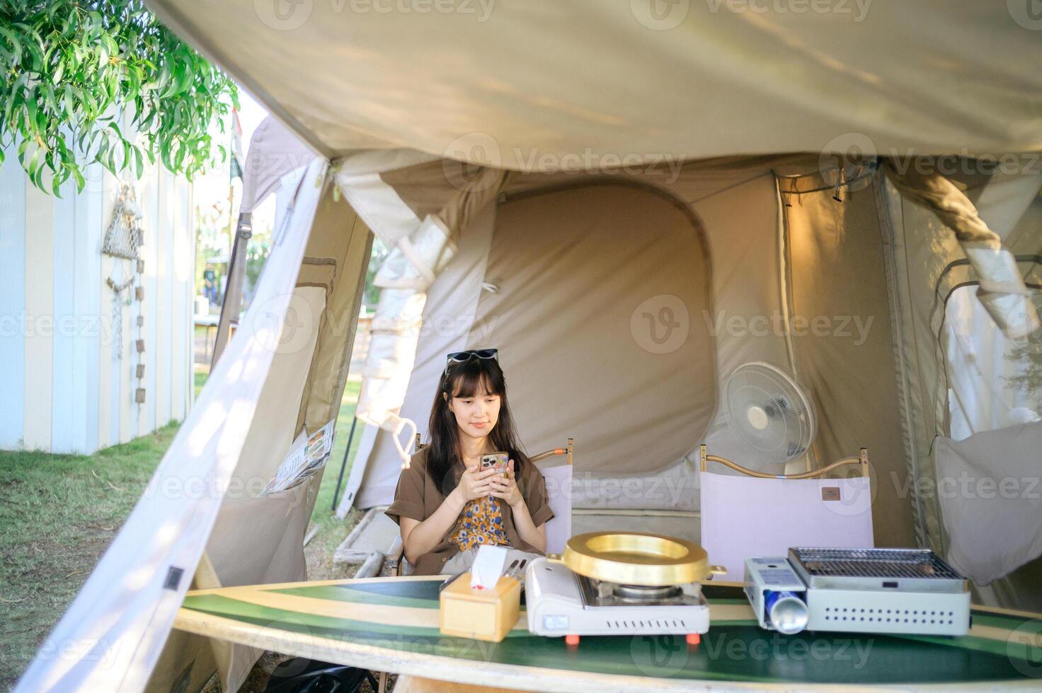 Southeast asian woman travel concept with young woman sitting inside tent enjoying her phone in relaxed outdoor setting photo
